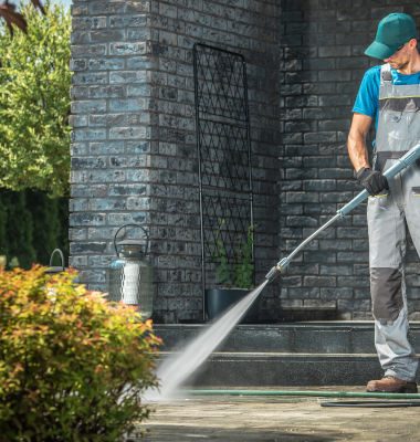 Maintenance worker cleaning porch area in front of the house using a jet hose.